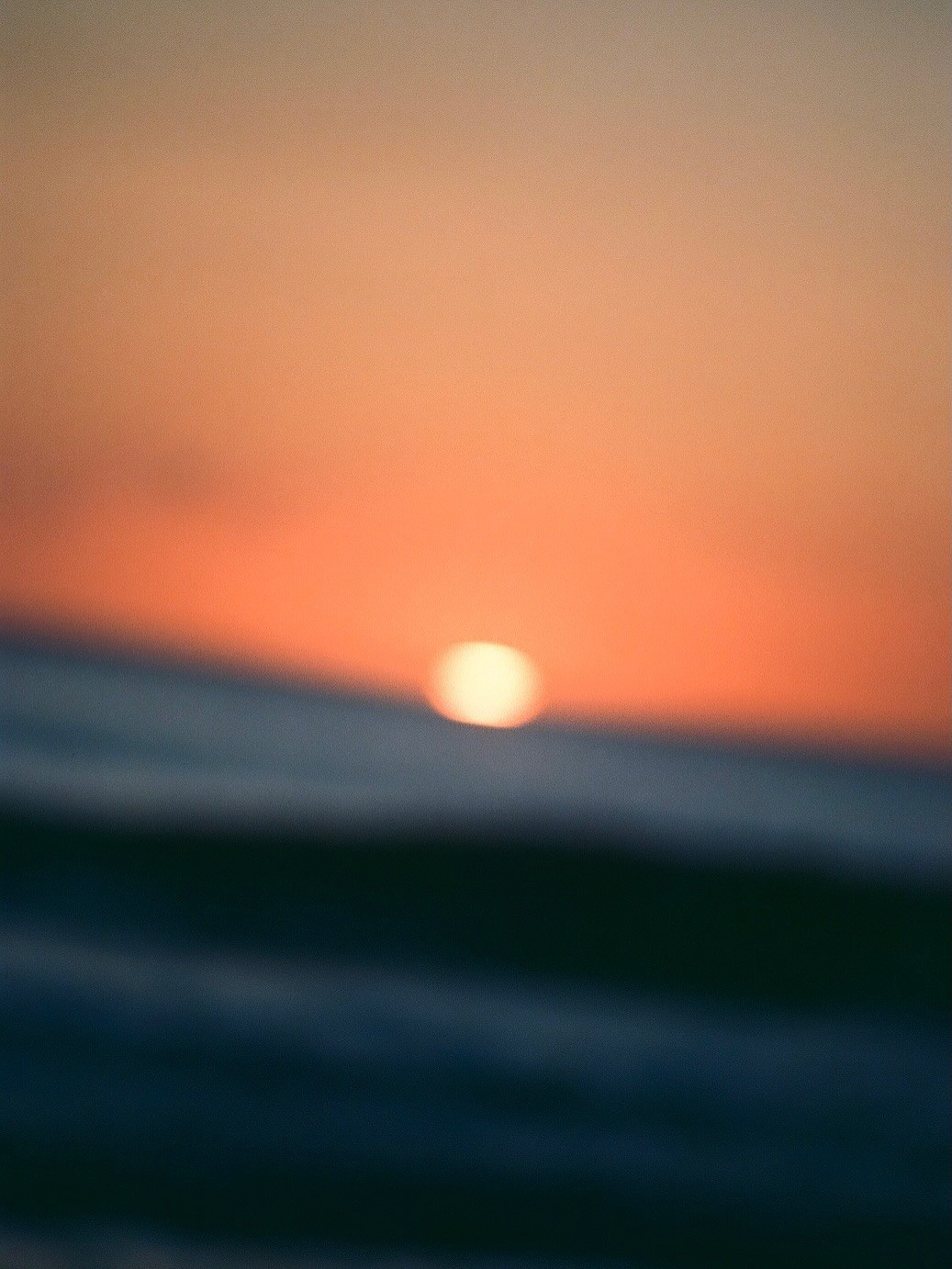 A blurred sunset glowing over dark ocean waves